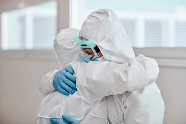 Medical Team in Protective Workwear Embracing in Support Male and female medical coworkers wearing protective suits, eyewear, and gloves hugging in support and recognition of hard work during COVID-19 pandemic. frontline worker stock pictures, royalty-free photos & images