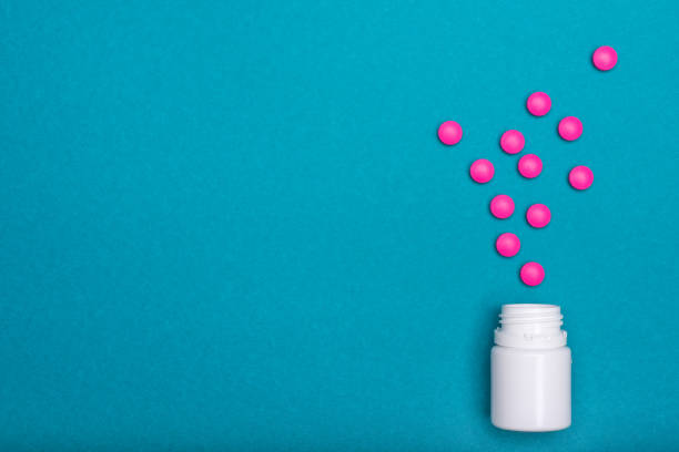 Medication bottle and bright pink pills spilled on dark blue coloured background. Medication and prescription pills flat lay background. Medication bottle and bright pink pills spilled on dark blue coloured background. Medication and prescription pills flat lay background. antihistamine stock pictures, royalty-free photos & images