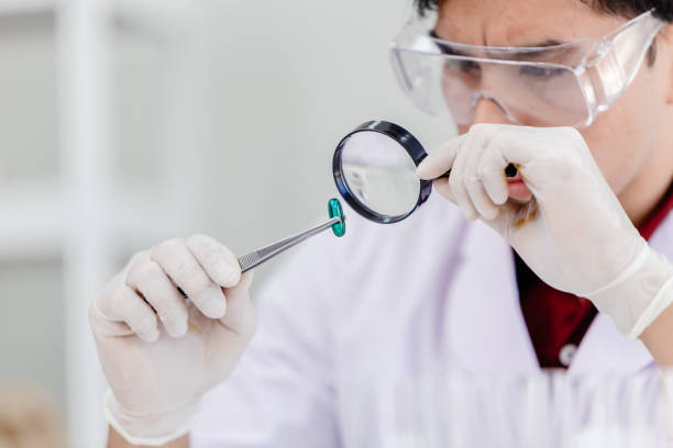 Medicine production quality assurance and care concept. Scientist in medical factory using magnifying glass to checking defective medical pill products. stock photo