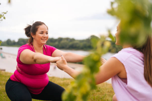 Medium shot of professional fitness female trainer giving personal training to overweight young woman outdoor in summer day. stock photo