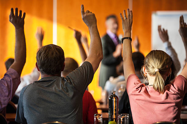Meeting attendees with raised hands in foreground stock photo