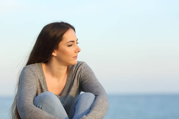 Melancholic woman looks away on the beach Melancholic woman complaining looking away sitting on the beach divorce beach stock pictures, royalty-free photos & images