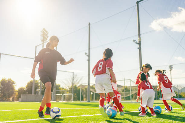 Members of female kids' soccer and football team training and dribbling to improve their skills stock photo