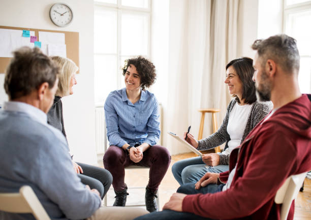 Men and women sitting in a circle during group therapy, talking. Serious men and women sitting in a circle during group therapy, talking. drug rehab stock pictures, royalty-free photos & images