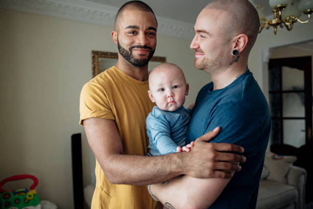 Men at Home With Their Son Two men spending time  with their little baby boy. They're all together at home standing in an embrace gay person stock pictures, royalty-free photos & images