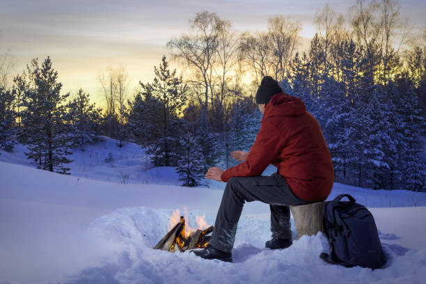 Men at sunset in the winter woods near a bonfire. Concept loneliness, of thinking men. stock photo