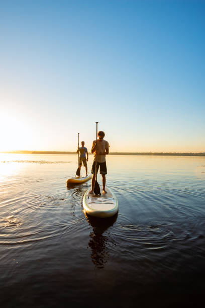Men, friends relax on a SUP boards during sunset stock photo