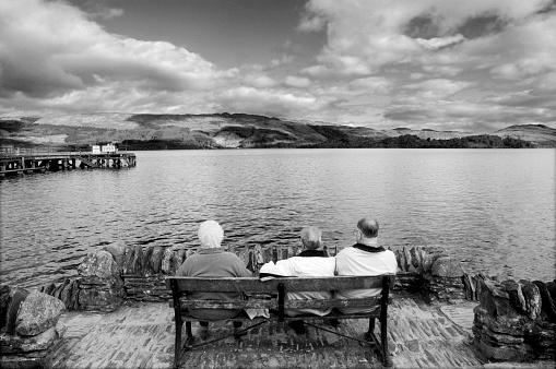 Luss, Scotland, UK - October 7, 2004: Three men sit on a bench in the village of Luss, Scotland by the pristine waters of Loch Lomond. Luss is a conservation village with picturesque cottages. In recent years, Luss became famous as a result of being the main outdoor location for the Scottish Television drama series Take the High Road. Loch Lomond is the largest loch/lake in Great Britain by surface area.