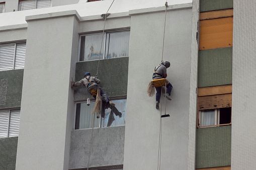 Men working on cleaning the facade of a building in São Paulo. Hanging by ropes on top of building. Maintenance concept. Building concept.