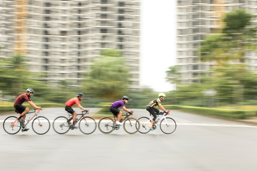 A group of male bicycle racers ride together during a criterium road bike race. A criterium road bike race is an event where competitors do several laps around a closed circuit usually in a city or urban center.