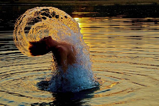 Merman Young adult male rising out of the water surrounded by water backlit by the sunset. merman stock pictures, royalty-free photos & images