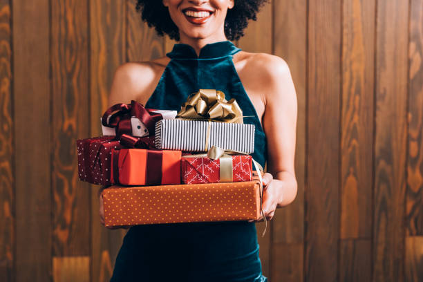 merry christmas: a n anonymous smiling elegant african american woman holding a pile of presents in her hands, a close up - woman holding a christmas gift imagens e fotografias de stock