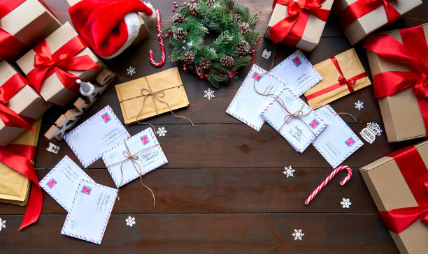 merry christmas decorated wooden table with post mail letters envelopes and gifts boxes, presents with red ribbons. xmas santa office desk workplace background concept. top view from above, flat lay. - a letter to santa claus, christmas gifts imagens e fotografias de stock