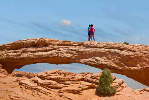 Standing on Mesa Arch Canyonlands National Park, Utah, USA - May 17, 2012: Mesa Arch is a pothole arch on the eastern edge of the Island in the Sky Mesa. This couple is looking at the view from the top of the famous arch. jeff goulden canyonlands national park stock pictures, royalty-free photos & images