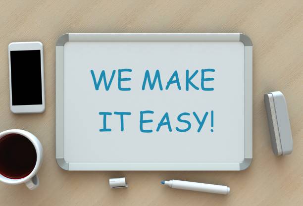 WE MAKE IT EASY!, message on whiteboard, smart phone and coffee on table stock photo