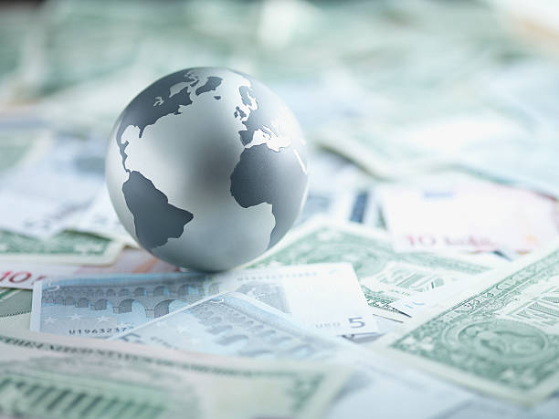metal globe resting on paper currency - küresel stok fotoğraflar ve resimler