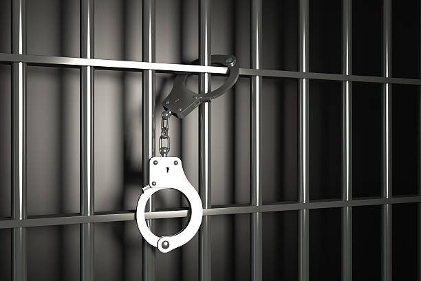 metal prison bars with handcuffs on black background stock photo