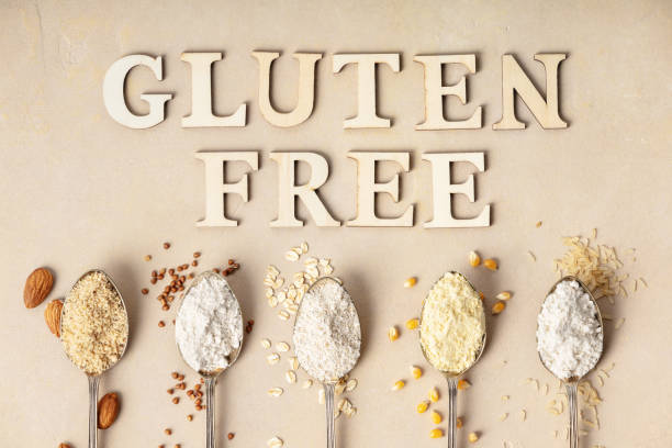 Metal spoons of various gluten free flour (almond flour, oatmeal flour, buckwheat flour, rice flour, corn flour) and gluten free lettering made of wooden letters, flat lay, top view stock photo