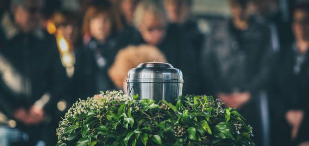 Metal urn at a funeral A metal urn with ashes of a dead person on a funeral, with people mourning in the background on a memorial service. Sad grieving moment at the end of a life. Last farewell to a person in an urn. ash stock pictures, royalty-free photos & images