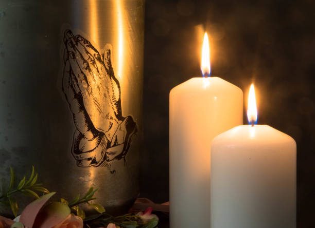 A metal urn with praying hands and burning candles with ashes from a dead person at a funeral. Sad grieving moment at the end of a life. Last farewell. Funeral and mourning concept. Mortuary urn with praying hands, burning candles and flowers against dark background Churches and funeral concept. Funeral symbol. Mourn and Condolence card concept. End of life. funerary urn stock pictures, royalty-free photos & images