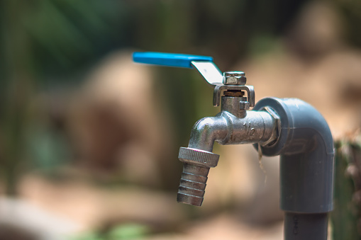 Metal water tap spigot stainless steel faucet lever ball valve blue handle connected to adapter manatee pipe. Blur background. Garden nature work plumbing. Copy space close-up real life style photo.