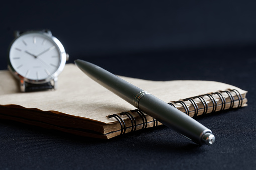 Metalized ballpoint pen and a spring-loaded notebook lie next to the wristwatch. Concept of will, notary, memoir and deadline. Selective focusing. Macro