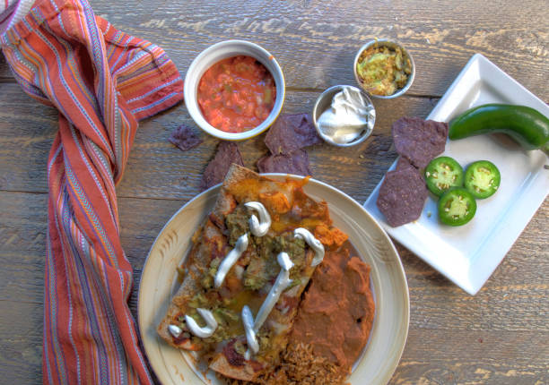 Mexican enchilada dinner with chips salsa and jalapenos on natural wood table top view stock photo