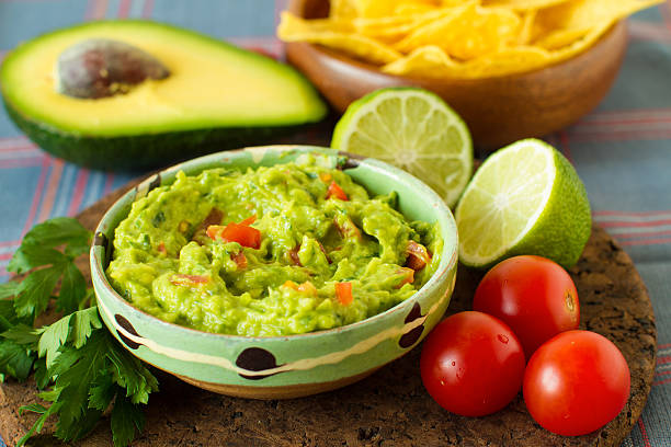 Mexican food: avocado dip A delicious traditional bowl of guacamole next to fresh ingredients on a table with tortilla chips and salsa tasty guacamole stock pictures, royalty-free photos & images