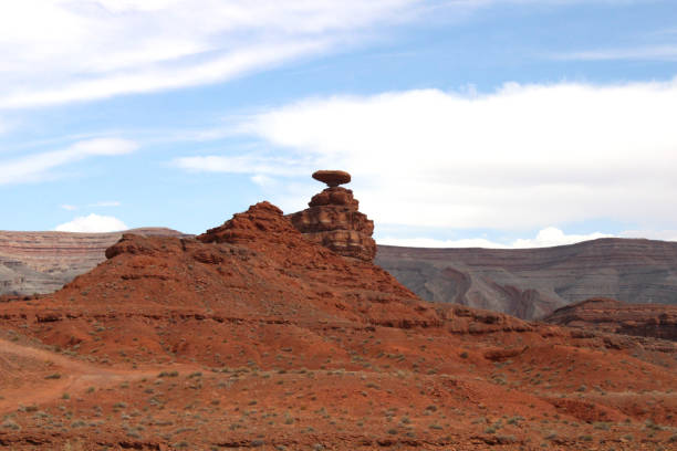 Mexican Hat Rock Formation in Utah Desert with Blue Sky and White Clouds in Background stock photo