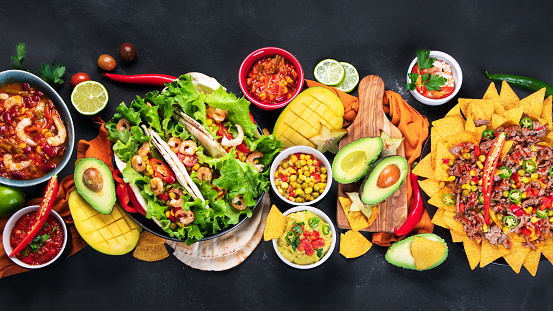 Mexican meal board with nachos, tacos, guacamole, shrimps, avocado and starfruit. Hot and spicy. Top view, copy space