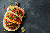 Mexican tacos with beef, vegetables and salsa. Tacos al pastor on wooden board on black background. Top view with copy space.