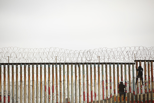 Tijuana, Baja California, Mexico - April 11, 2021: Individuals scale the Mexico side of the USA Mexico border wall.