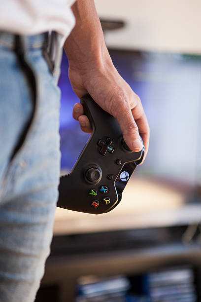 Microsoft Xbox One - Game Controller Gothenburg, Sweden - June 21, 2015: A shot of a young man's hand holding a Xbox One game controller, a remote controller for the Xbox One video game console developed and released by Microsoft in 2013. Natural lighting. Shot in a home bedroom with a TV in the background. xbox photos stock pictures, royalty-free photos & images