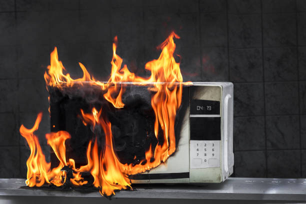 Microwave oven burns, house fire due to improper operation, spontaneous combustion of faulty appliances Microwave oven white, in fire front view, electrical appliances caught fire as a result of improper operation microwave stock pictures, royalty-free photos & images