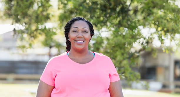 Mid adult African-American woman A mid adult African-American woman, in her 30s, with braided hair, wearing a pink t-shirt. She is smiling and looking at the camera. voluptuous women images stock pictures, royalty-free photos & images