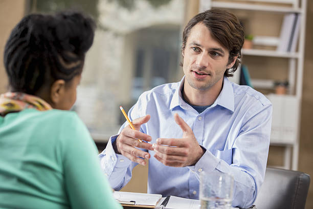 Mid adult businessman interviews potential employee Confident mid adult Caucasian manager interviews prospective African American female employee. The man is gesturing while talking. The woman's back is to the camera. alertness photos stock pictures, royalty-free photos & images