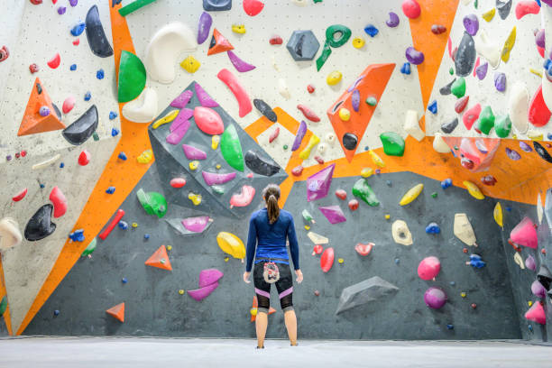 Mid adult caucasian brunette woman looking at indoor artificial climbing wall Back view of mid adult caucasian brunette woman in sport suit looking at indoor artificial climbing wall. Various colors and shapes of grips for hands and feet. bouldering stock pictures, royalty-free photos & images