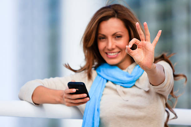 Mid adult female holding cellphone and giving okay sign stock photo