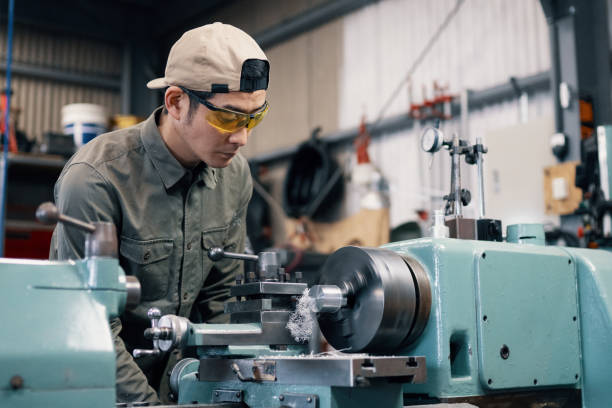 Mid adult male using a lathe to machine a piece of metal stock photo