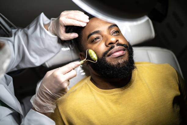 mid adult man receiving a facial massage at a spa - schoonheidsspecialist stockfoto's en -beelden