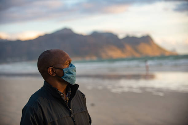 средний взрослый человек с маской на пляже и горном фоне, глядя в сторону - south africa covid стоковые фото и изображения
