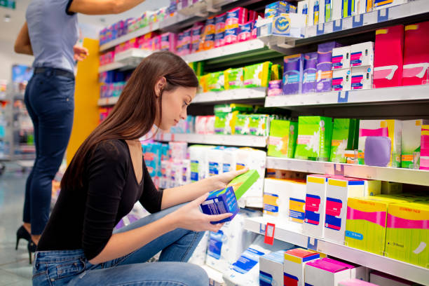 Mid adult woman crouching and choosing sanitary pads Mid adult woman crouching and taking time choosing sanitary pads in pharmacy aisle photos stock pictures, royalty-free photos & images