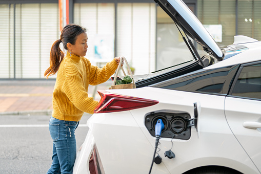 Mid adult woman loading groceries into her electric car. Okayama, Japan. 2021