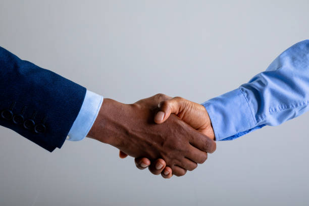 Mid section of two businessman shaking hands against grey background stock photo