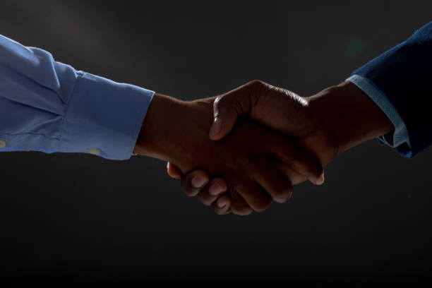 Mid section of two businessmen shaking hands against black background stock photo