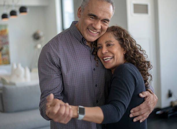 A middle age couple laughing and dancing together A couple smile as they dance together in their lounge room. The middle age women is of African descent and is resting her head on her husbands chest.  They are holding each other close and appear happy and relaxed. old black couple in love stock pictures, royalty-free photos & images