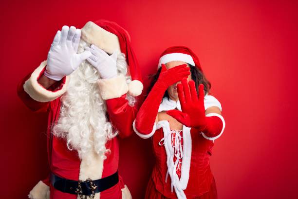 Middle age couple wearing Santa costume and glasses over isolated red background covering eyes with hands and doing stop gesture with sad and fear expression. Embarrassed and negative concept. Middle age couple wearing Santa costume and glasses over isolated red background covering eyes with hands and doing stop gesture with sad and fear expression. Embarrassed and negative concept. embarrassment photos stock pictures, royalty-free photos & images