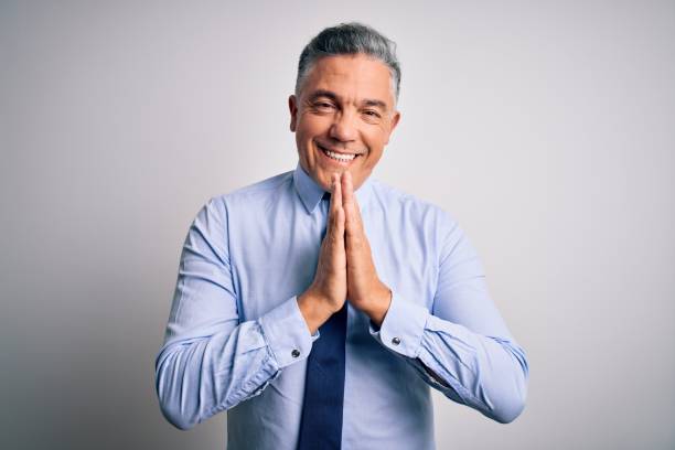 Middle age handsome grey-haired business man wearing elegant shirt and tie praying with hands together asking for forgiveness smiling confident.  prayer request stock pictures, royalty-free photos & images