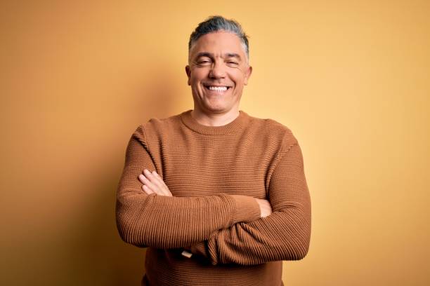 Middle age handsome grey-haired man wearing casual sweater over yellow background happy face smiling with crossed arms looking at the camera. Positive person. Middle age handsome grey-haired man wearing casual sweater over yellow background happy face smiling with crossed arms looking at the camera. Positive person. sweater photos stock pictures, royalty-free photos & images