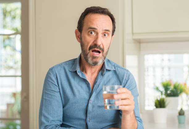 Middle age man drinking a glass of water scared in shock with a surprise face, afraid and excited with fear expression Middle age man drinking a glass of water scared in shock with a surprise face, afraid and excited with fear expression worried man funny stock pictures, royalty-free photos & images